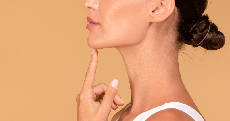 Nahaufnahme eines markanten weiblichen Kinns mit straffer Jawline auf beigem Hintergrund