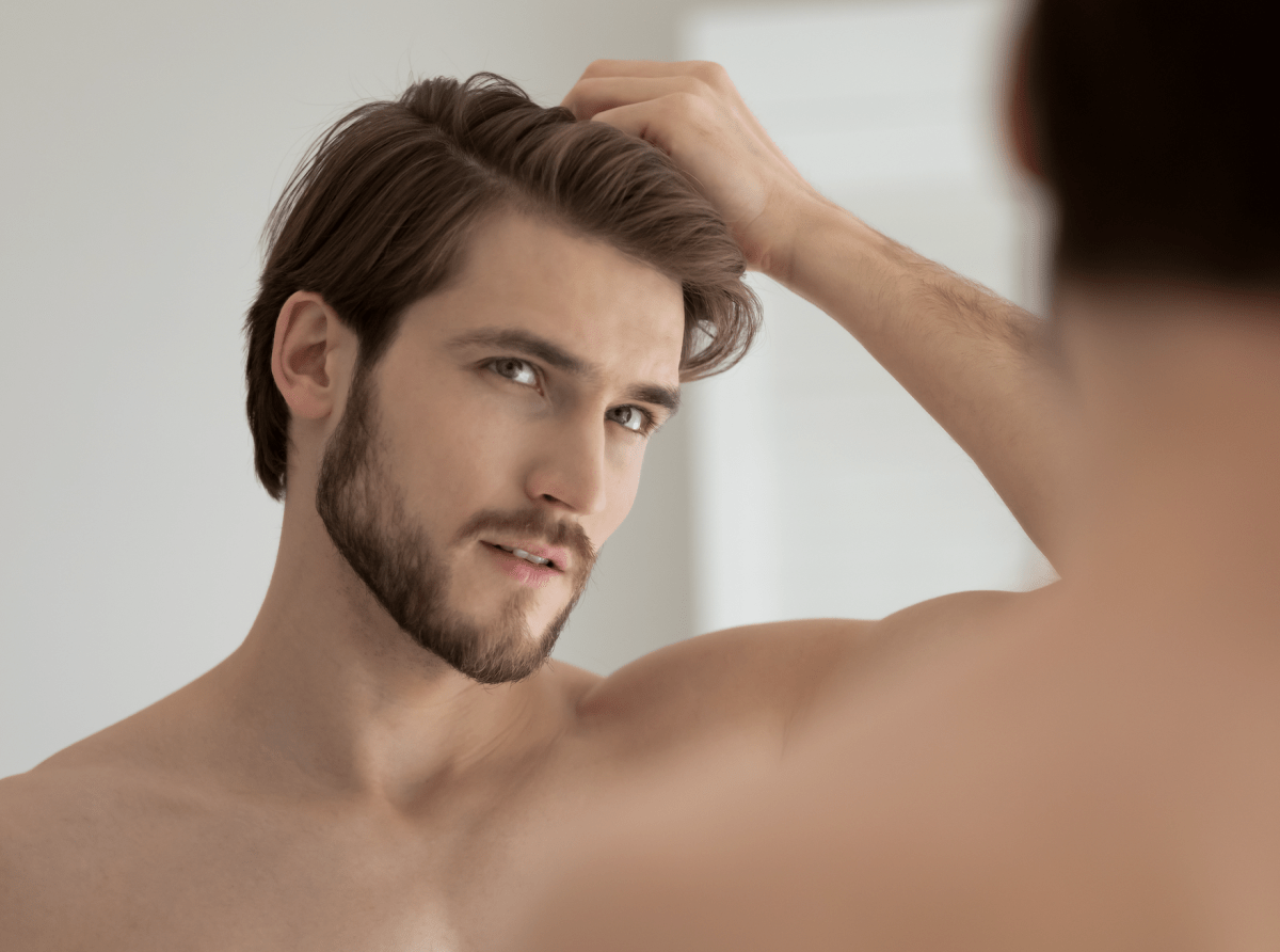 Junger Mann prüft Haaransatz vor dem Spiegel – Thema Haargesundheit und Haarbehandlung bei MYH&amp;B