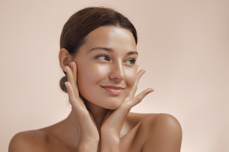 Junge Frau mit strahlender Haut betont ihr Gesicht mit beiden Händen