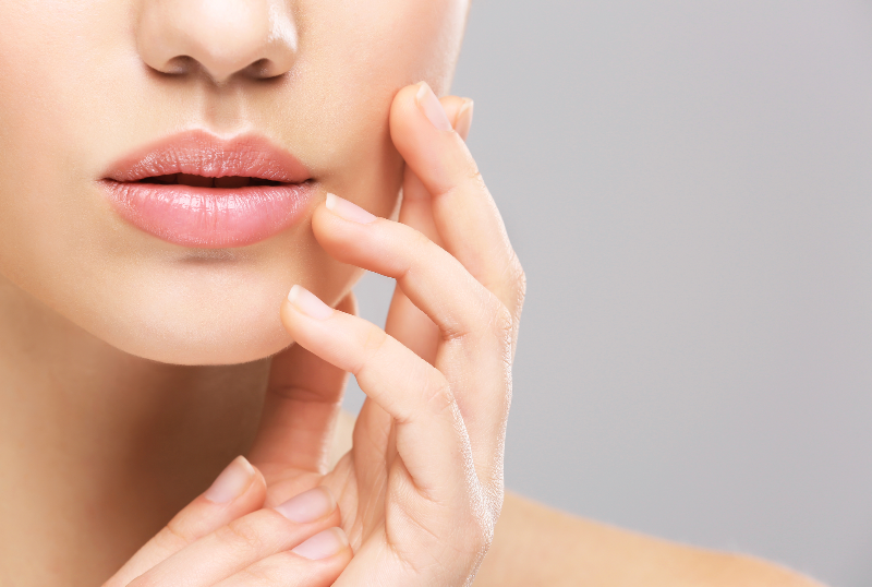 Nahaufnahme weiblicher Lippen und Hand – Symbol für ästhetische Lippenbehandlungen und Pflege.