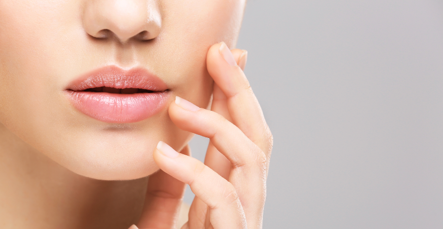 Nahaufnahme der Lippen und Wange einer Frau mit makelloser Haut, die ihr Gesicht berührt.