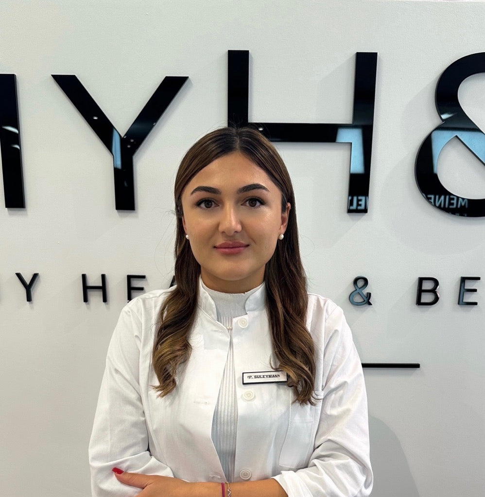 MYH&B Ärztin im weißen Kittel mit Namensschild „Dr. Suleyman“ vor Logo-Wand