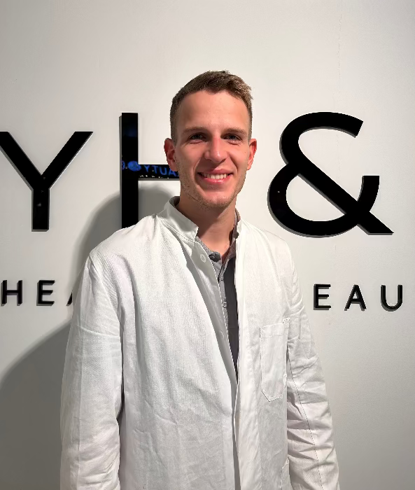 Männlicher Arzt bei MYH&B im weißen Kittel vor Markenlogo – freundlich und kompetent