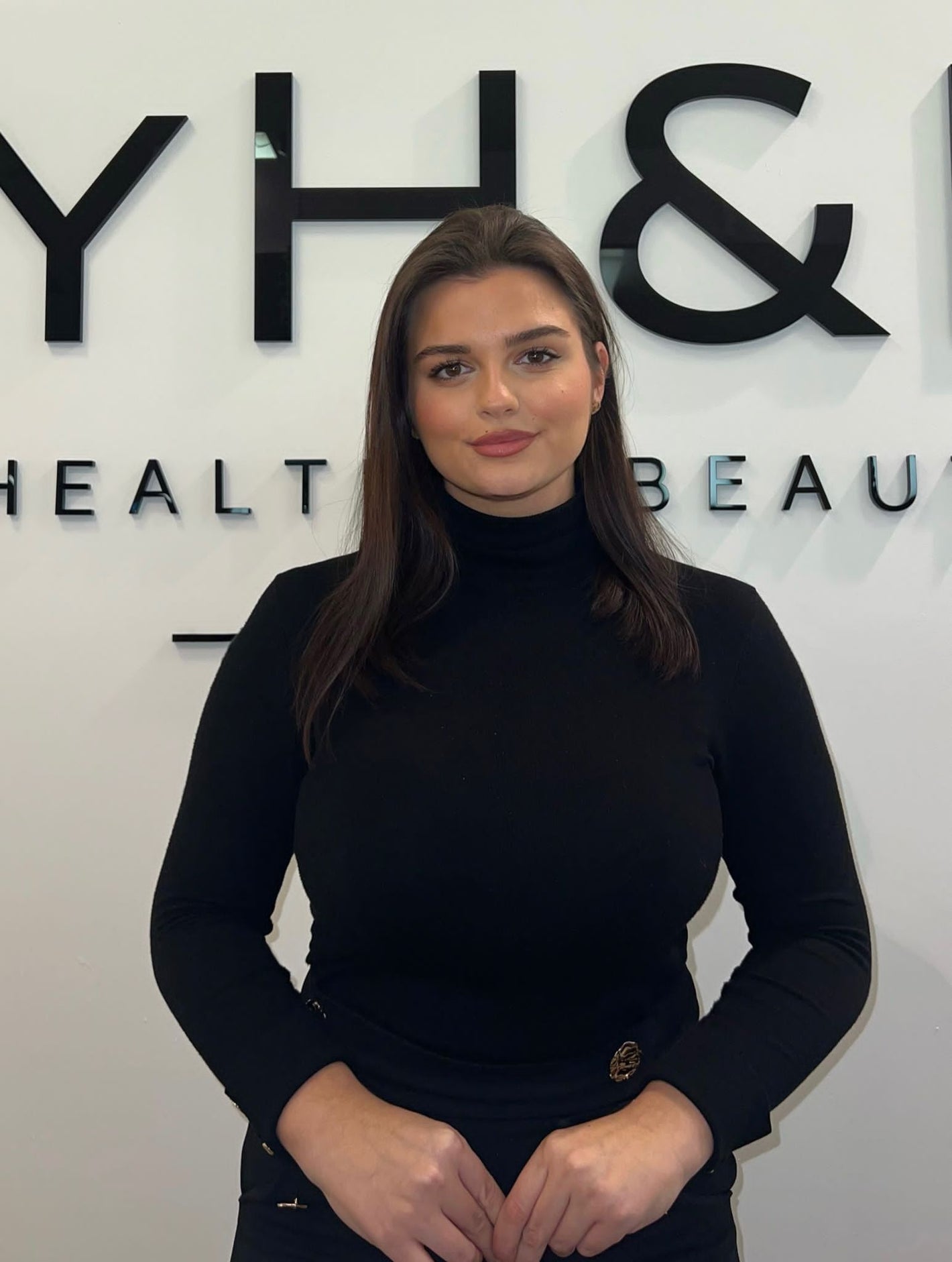 Teammitglied von MYH&B mit dunklen Haaren und schwarzem Outfit vor Praxislogo