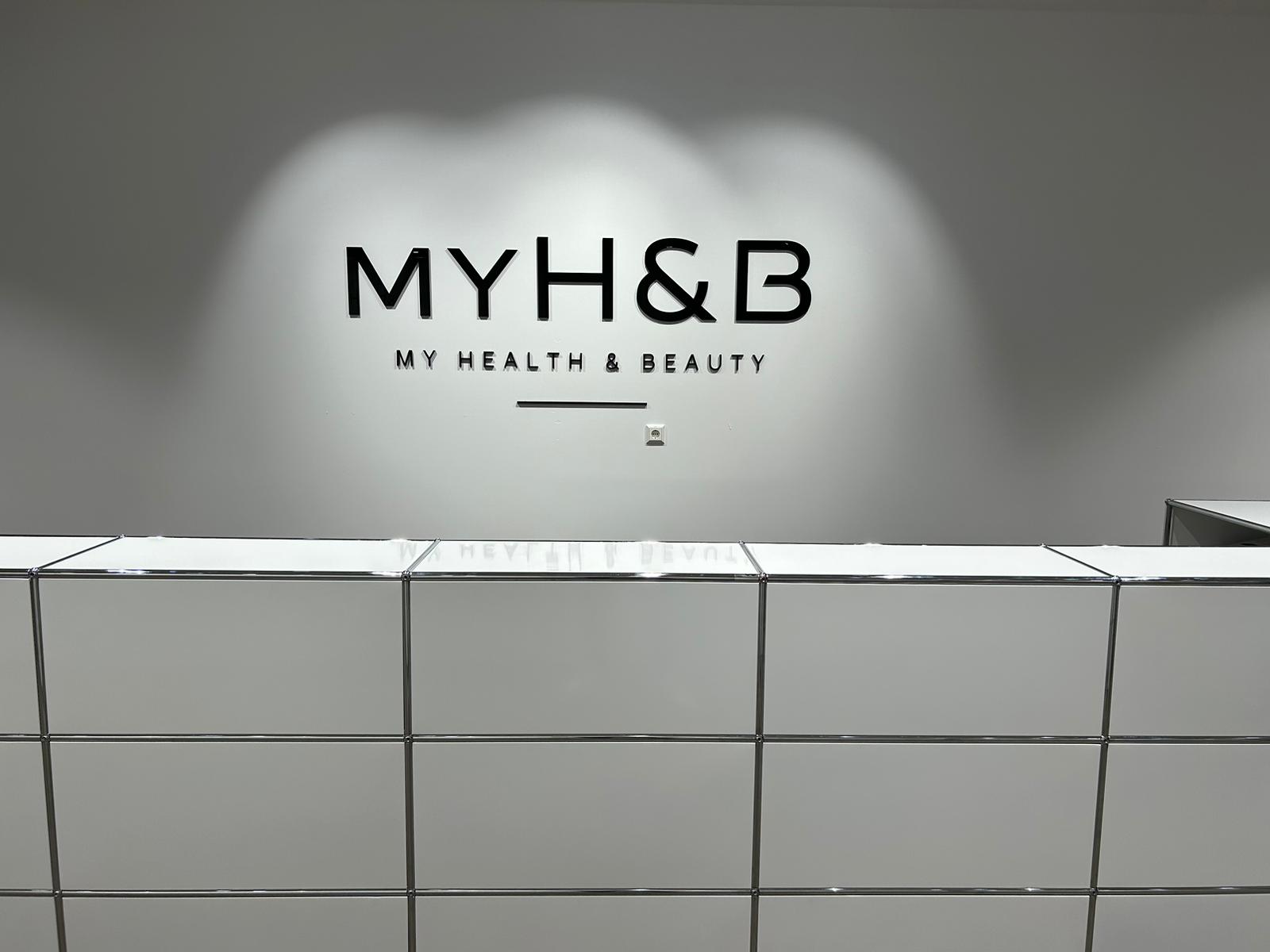 Minimalistischer Empfangsbereich bei MYH&B mit weißer Theke und Logo an der Wand.