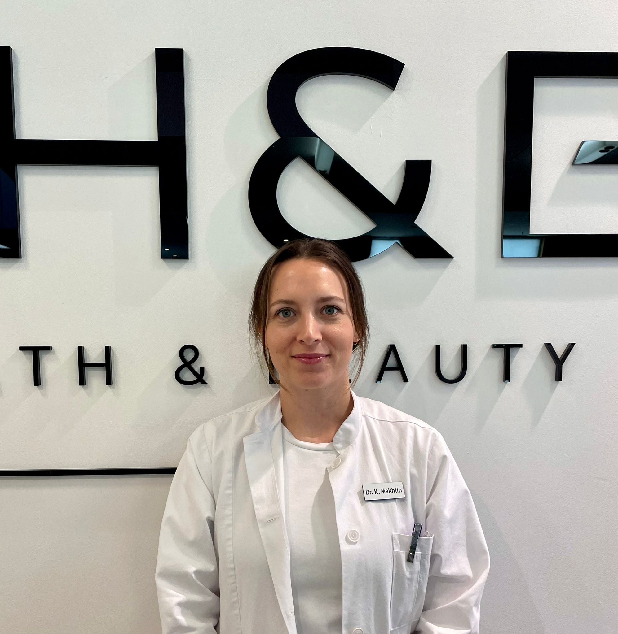 Ärztin in weißem Kittel vor MYH&B Logo – moderne, professionelle Ausstrahlung in der Praxis